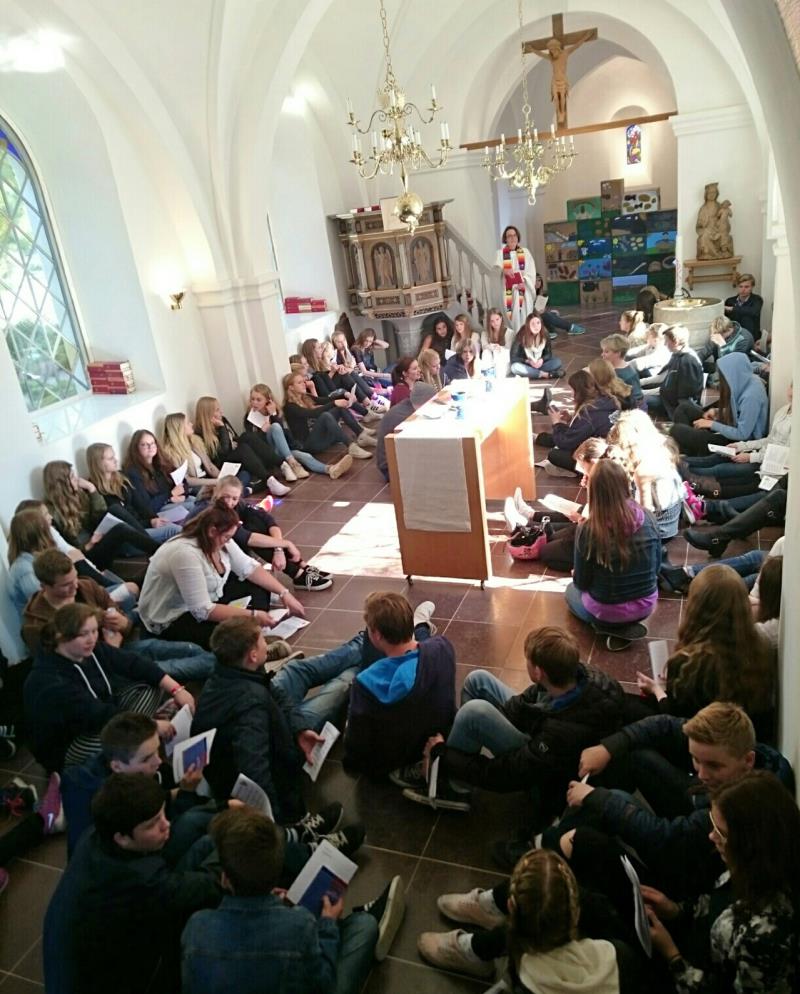 Inga stolar i Brågarps kyrka, konfirmander och ledare sitter golvet runt ett flyttbart altare i mitten av kyrkorummet.