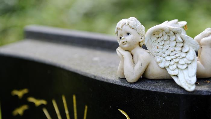 En ängel i sten ligger på mage på en gravsten, på gravstenen syns inristade fåglar och streck i guld.