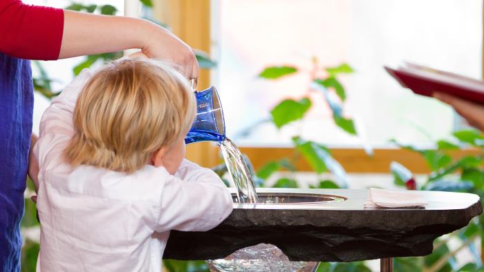 Ett barn häller upp vatten i en dopfunt.