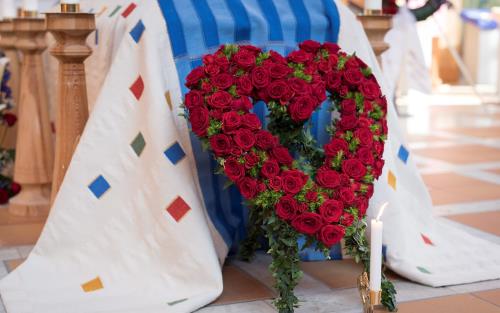 En begravningskrans i form av ett stort hjärta med rosor vilar mot en kista.