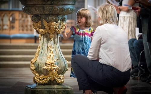 Kvinna på huk framför flicka i en kyrka.