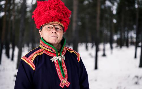 Man i nordsamisk dräkt står i vintrigt landskap.