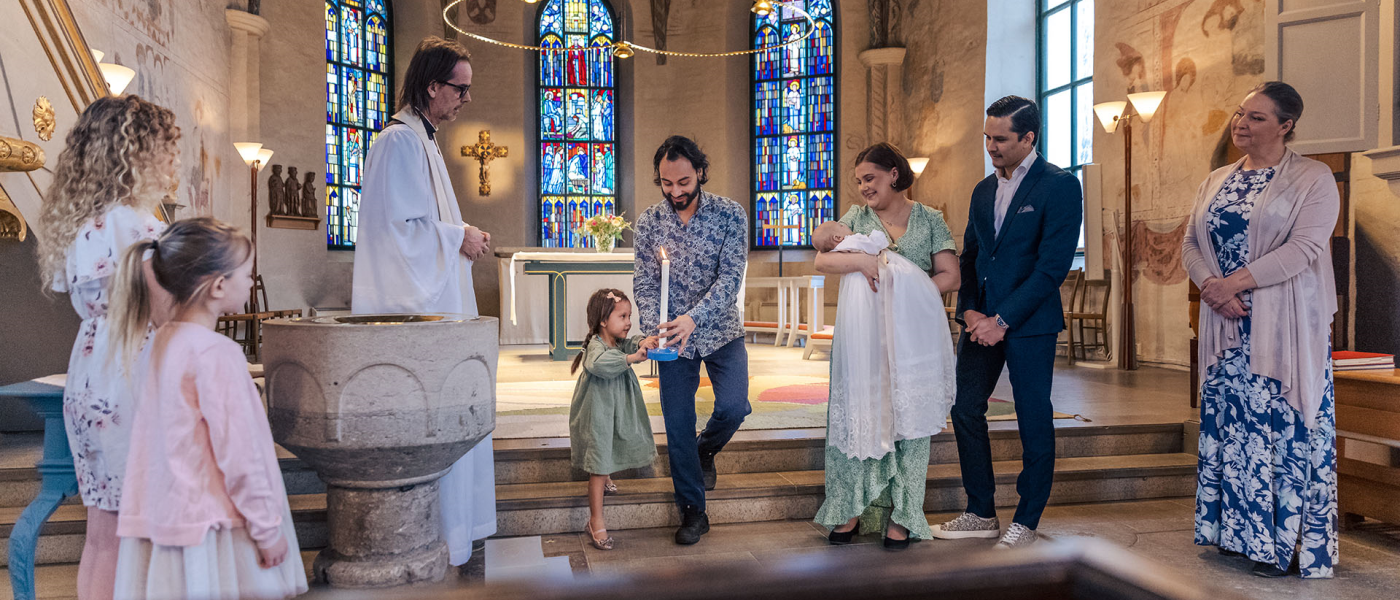 En glad dopfamilj, faddrar och präst står långt fram i kyrkan.