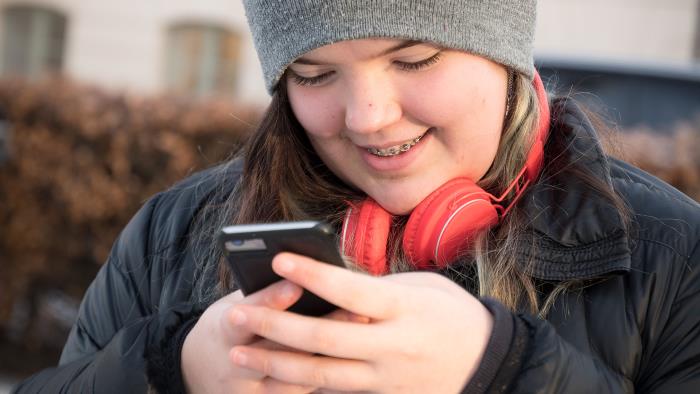 En ung tjej med röda hörlurar knappar in ett nummer på mobiltelefonen.