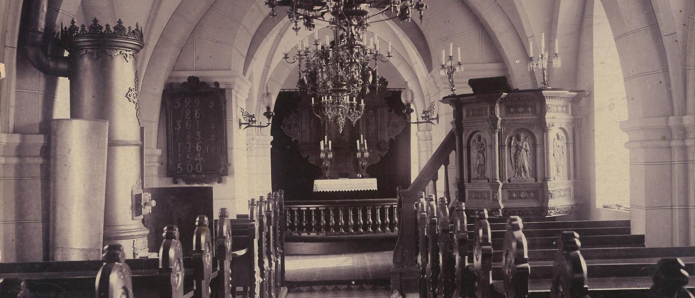Brågarps kyrka invändigt med kamin vid norrväggen, predikstolen vid söderväggen, stor altaruppsats och bänkar i mörkt trä.
