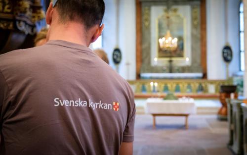 Person i grå T-shirt med Svenska kyrkan-logga i ett kyrkorum