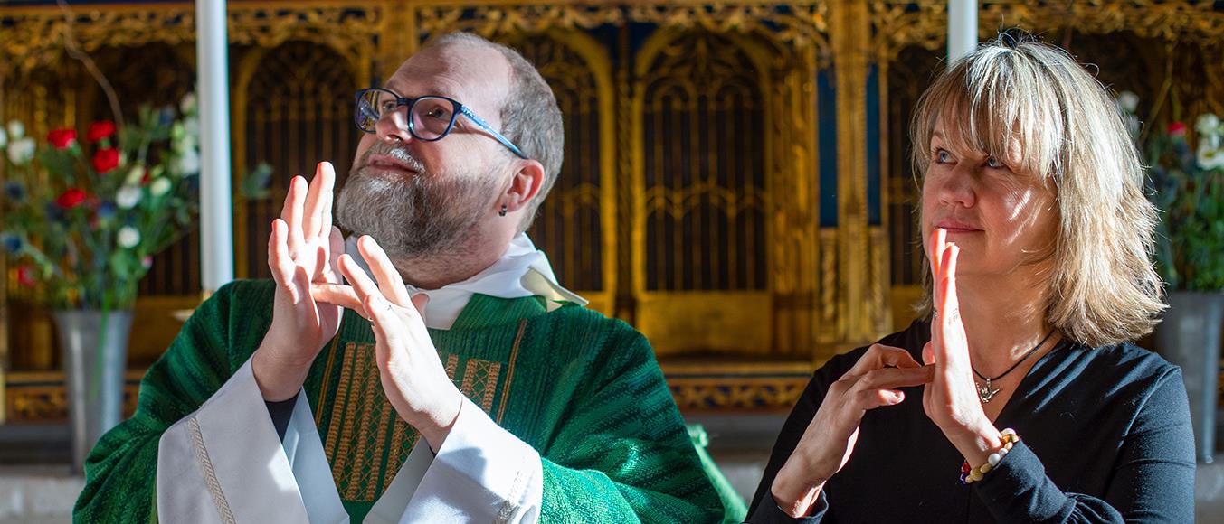 Dövpräst Johan Wisser och stiftskonsulent Åsa Grönberg står vid altare och använder teckenspråk.