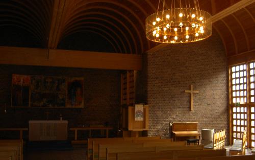 Interiörbild från Almtunakyrkans kyrkorum med dagsljus från höger som dfaller över inredningen och ett väggkors i trä.