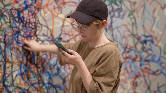 Vi ser konstnären Johanna Hästö blindteckna live på en vägg utifrån mobilfoton, utan att titta på teckningen medan den framträder. 