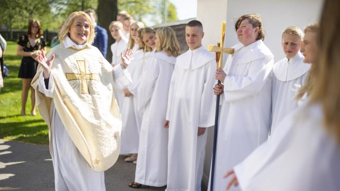 En präst hälsar på en konfirmand utanför en kyrka