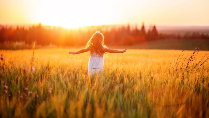 En flicka springer med utsträckta armar över ett gyllene sädesfält i solnedgång.