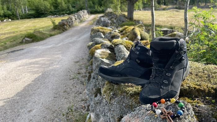 Vandringskängor står på en mur, bredvid en pilgrimskrans. 