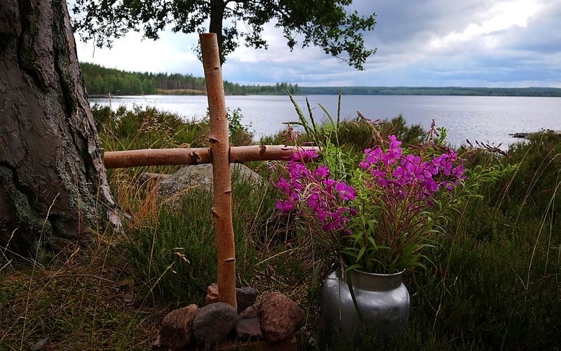 Enkelt kors och blommor vid strandkant