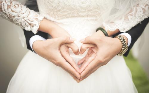 Man och kvinna håller sina händer i en hjärtsymbol i bröllopskläder.