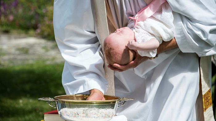 Präst håller spädbarn vid dop.