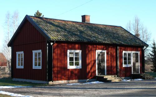 Litet rött hus med svarta knutar och vita fönsterfoder.
