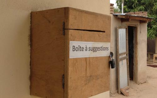 En låda med texten Boite a suggetions - förslagslåda sitter på en väg, i bakgrunden syns ett skjul.