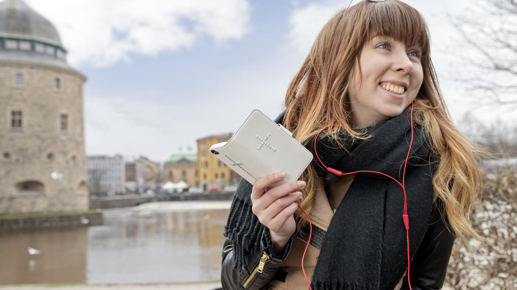 I förgrunden tjej som talar i telefonen. Hennes smartphone har ett mobilskal med ett strasskors på. I bakgrunden Örebro slott.