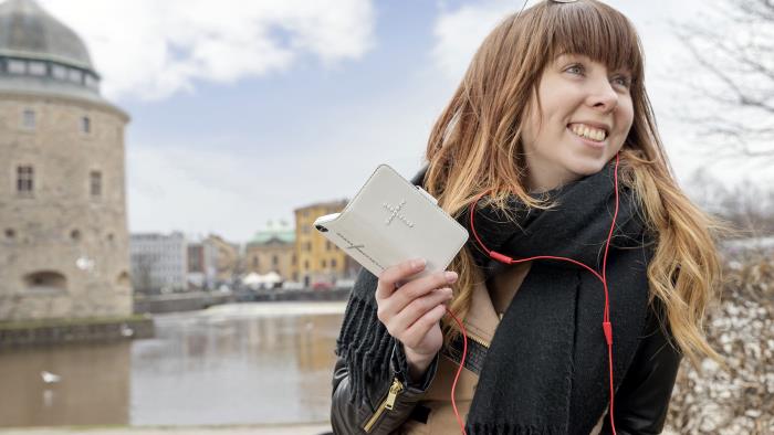 I förgrunden tjej som talar i telefonen. Hennes smartphone har ett mobilskal med ett strasskors på. I bakgrunden Örebro slott.