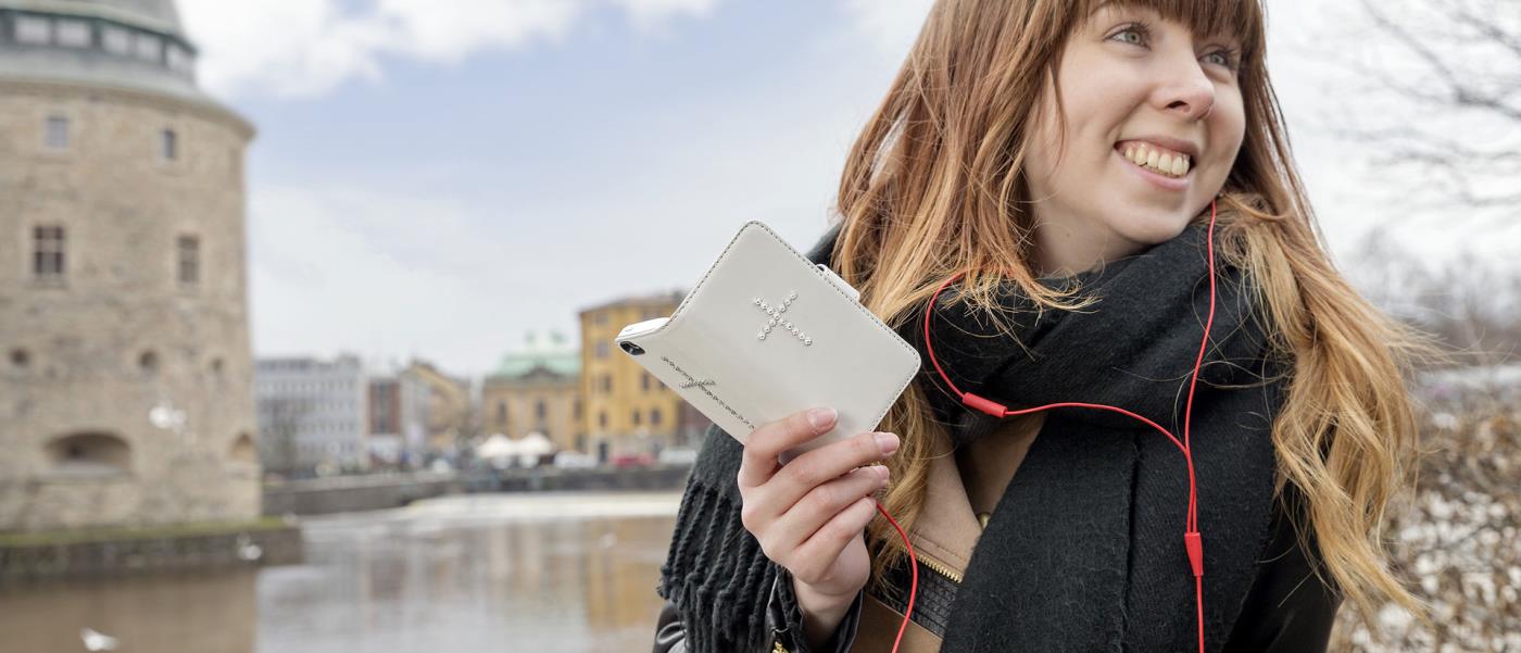 I förgrunden tjej som talar i telefonen. Hennes smartphone har ett mobilskal med ett strasskors på. I bakgrunden Örebro slott.