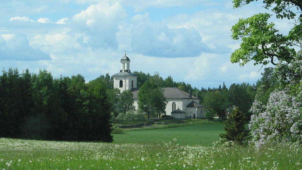 Huddunge kyrka med gräs och blommande träd i förgrunden.
