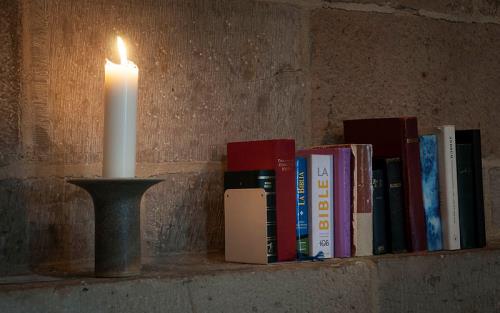 Tänt vitt ljus i ljusstake och biblar i nisch i kyrka.