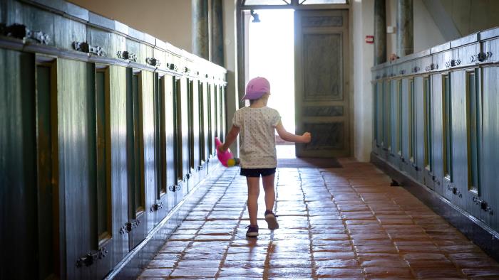 Litet barn i lila keps springer längs altargången i kyrkan mot den öppna kyrkporten.