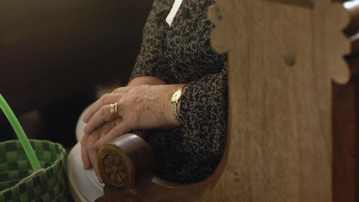 En kvinna sitter i kyrkbänken med händerna i knät.