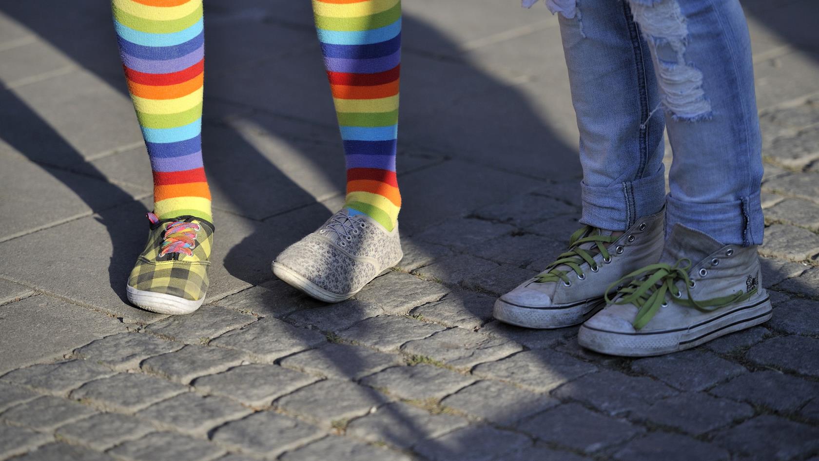 Två barn står bredvid varandra, bara benen syns. Den ena har regnbågsfärgade strumpbyxor.