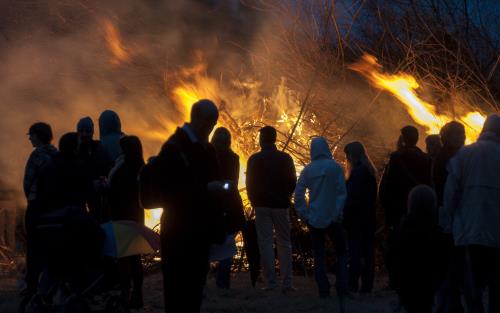 En grupp människor står vid en majbrasa i mörkret.