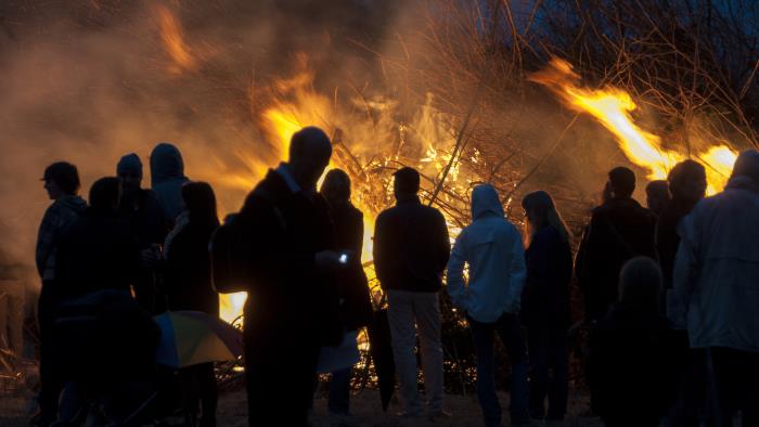 En grupp människor står vid en majbrasa i mörkret.