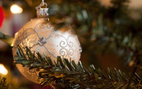 En vit julgranskula med glittriga detaljer hänger i granen.