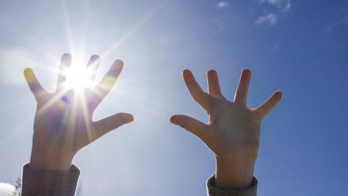 Ett barn sträcker upp händerna mot himlen. Solen lyser igenom fingrarna.