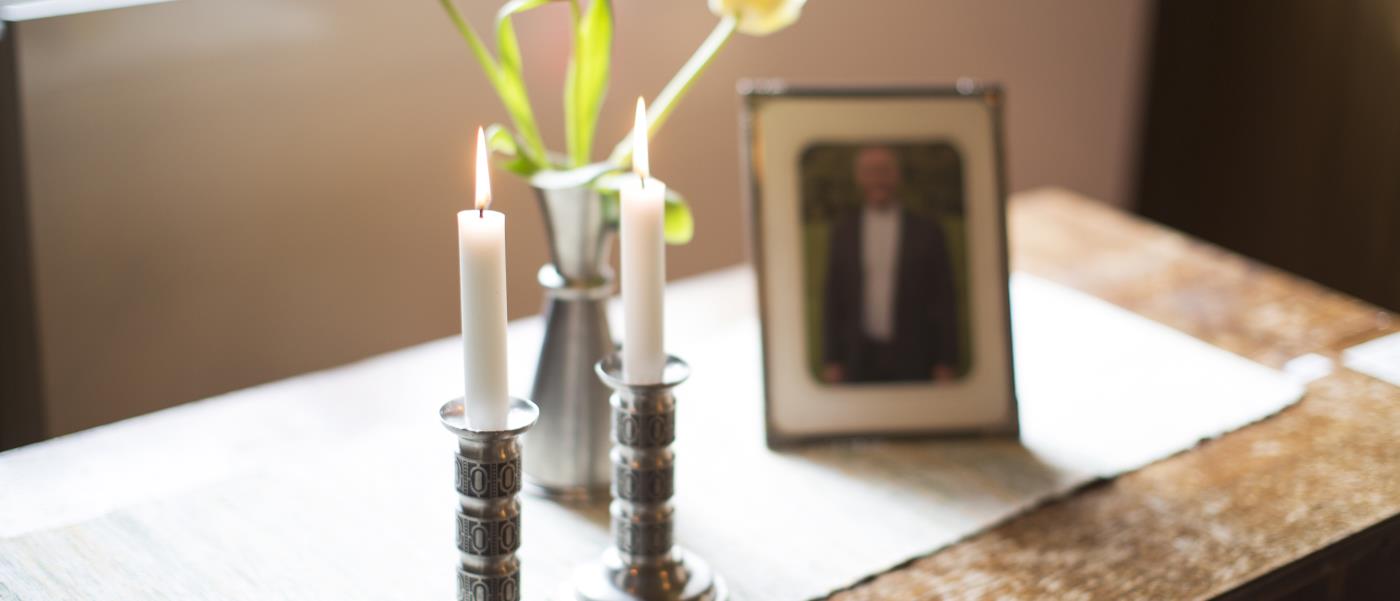 Två tända ljus, en vas med tulpaner och ett inramat fotografi står på ett bord.