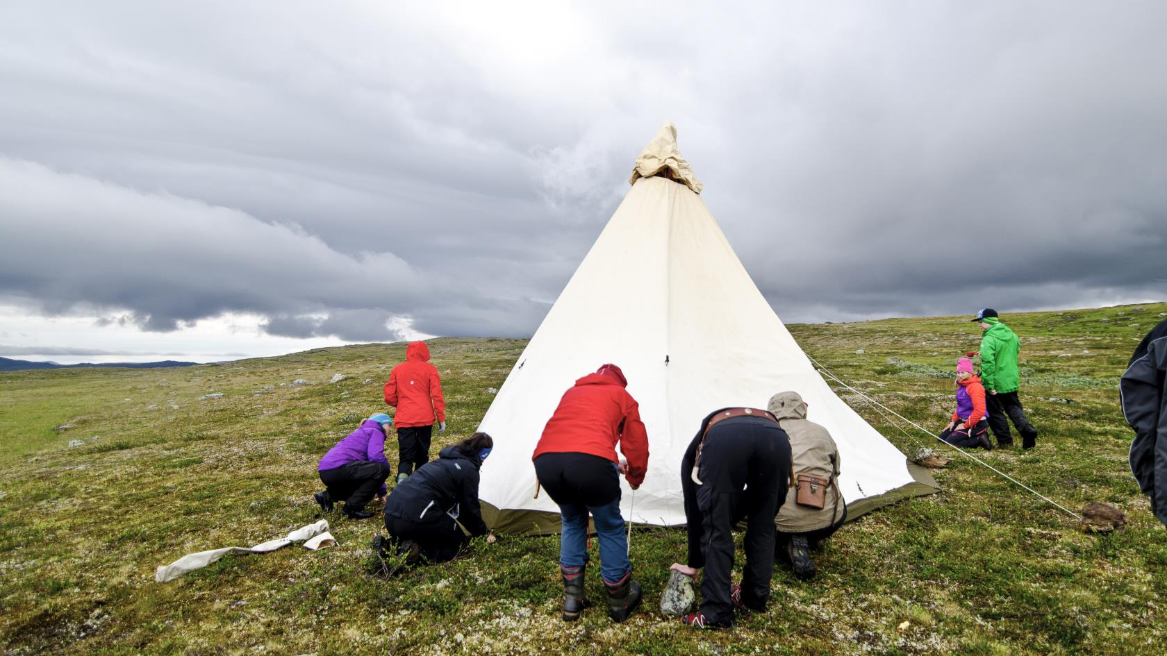 En grupp människor sätter upp ett tält på fjället.