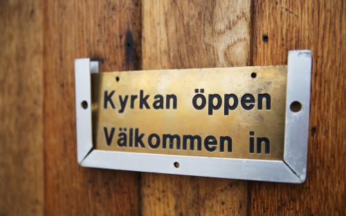 En skylt på en dörr med texten Kyrkan öppen välkommen in.