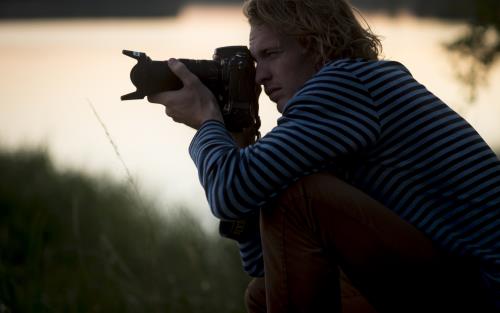 En man sitter ute i naturen och fotograferar.