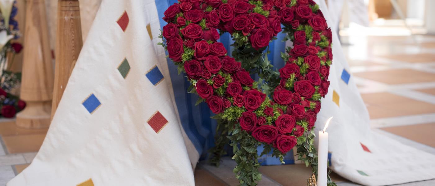 En begravningsbukett i form av ett hjärta av röda rosor står framför en kista.