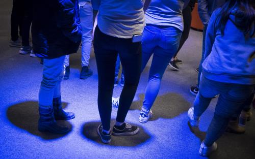 En grupp ungdomar står i ett rum med blått ljus som lyser ner på dem.