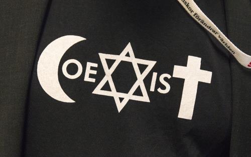 Symbolerna för islam, judendom och kristendom bildar tillsammans ordet Coexist på en tröja.