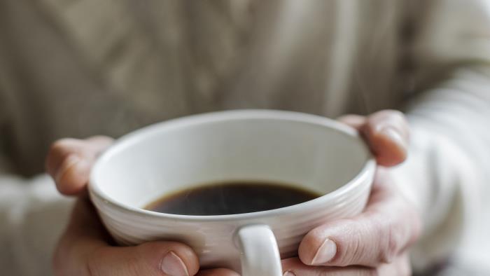 Någon håller händerna runt en kopp med kaffe.