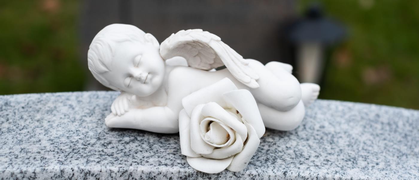 En liten sovande ängel i porslin ligger på en gravsten.