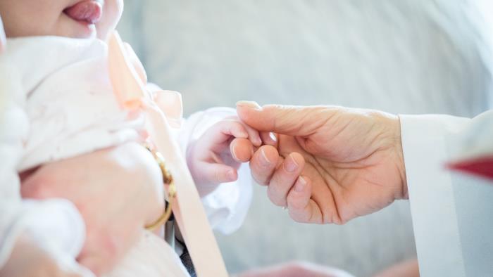 En vitklädd person håller i handen på en bebis i dopklänning.