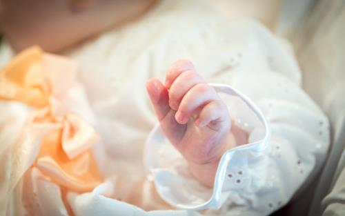 Närbild på en hand som tillhör en bebis i dopklänning.