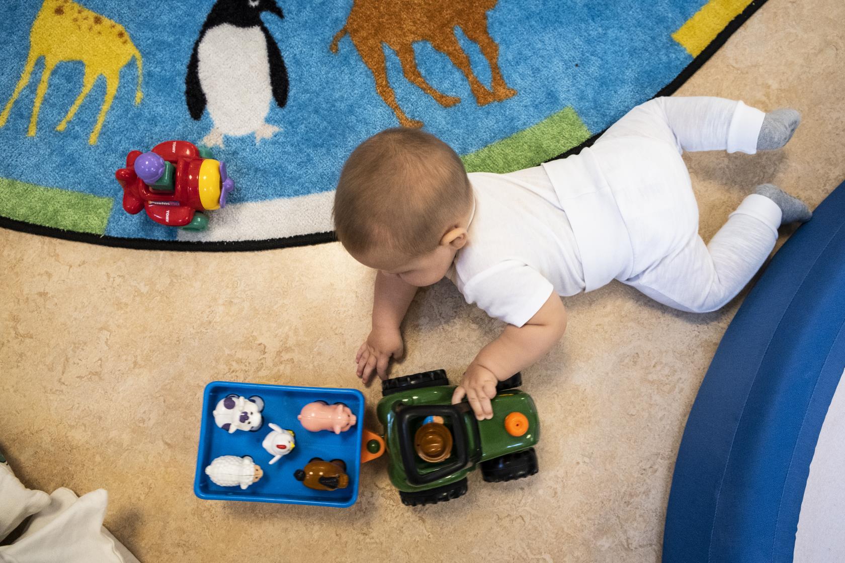 En bebis ligger på mage på golvet och leker med en traktor.