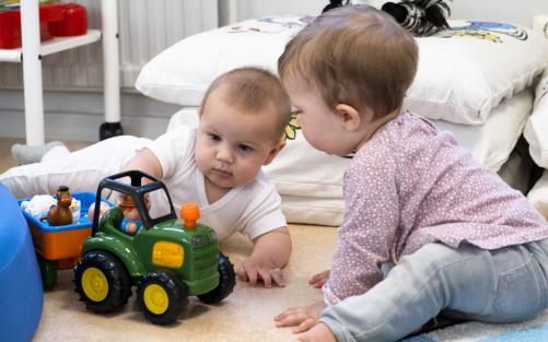 Två bebisar sitter på golvet och leker med en traktor med släpvagn.