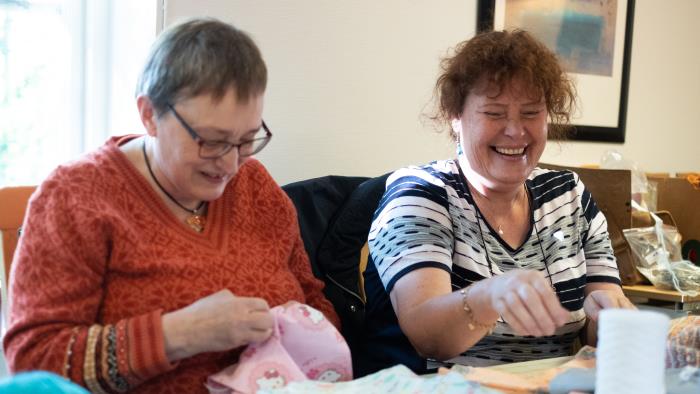 Två glada äldre kvinnor sitter bredvid varandra och syr.