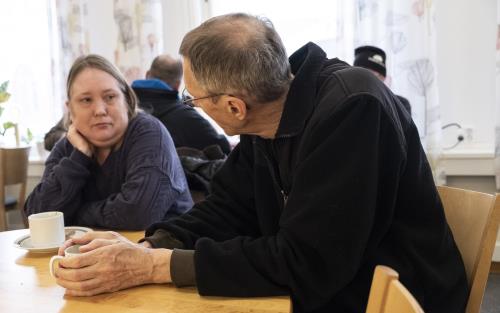 En man och en kvinna sitter vid ett bord och samtalar över en kopp kaffe.
