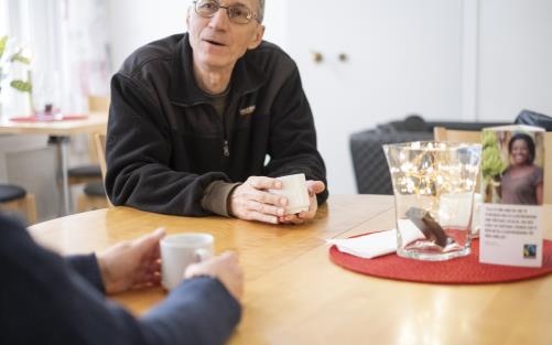 En man sitter och samtalar med någon över en kopp kaffe.