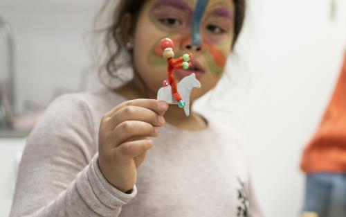 En flicka har en fjäril målad i ansiktet. Hon håller upp en gubbe gjord av piprensare.